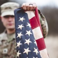 A selective focus shot of an American soldier holding the American flag close to the camera